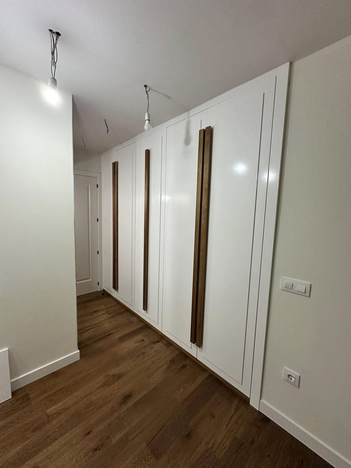 Armarios blancos con tiradores de madera y suelo de tarima.